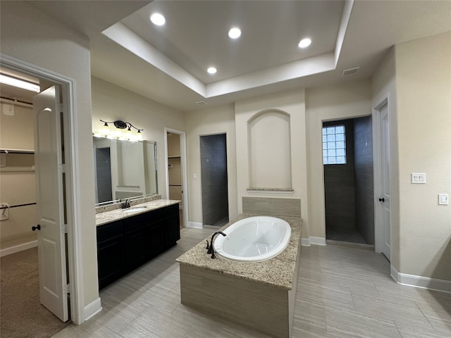 bathroom featuring independent shower and bath, vanity, and a tray ceiling