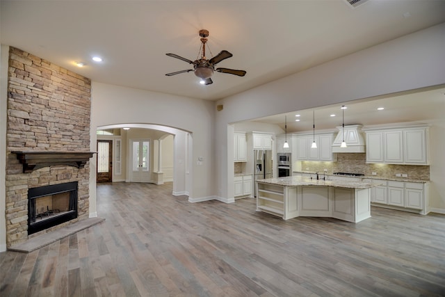 kitchen with light hardwood / wood-style floors, sink, custom exhaust hood, hanging light fixtures, and a kitchen island with sink