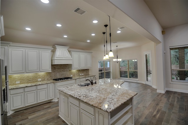 kitchen featuring dark hardwood / wood-style flooring, a center island with sink, sink, custom exhaust hood, and light stone countertops