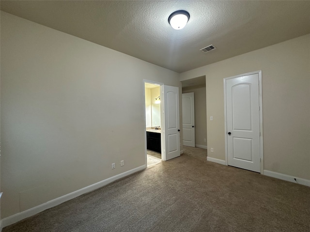 unfurnished bedroom with ensuite bathroom, carpet, a textured ceiling, and a closet