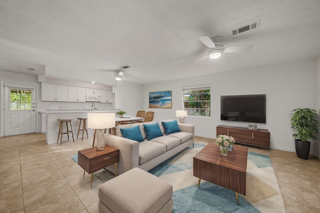 living room with a textured ceiling, ceiling fan, and light tile patterned floors