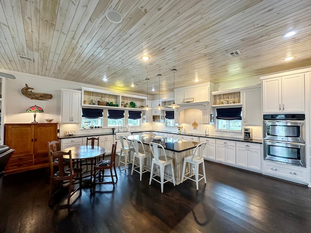 kitchen with double oven, dark hardwood / wood-style floors, pendant lighting, a breakfast bar, and wooden ceiling