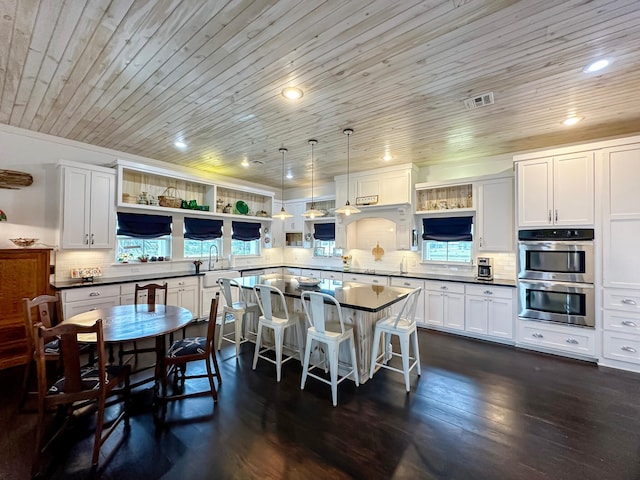 kitchen with white cabinetry, pendant lighting, a breakfast bar area, dark wood-type flooring, and double oven