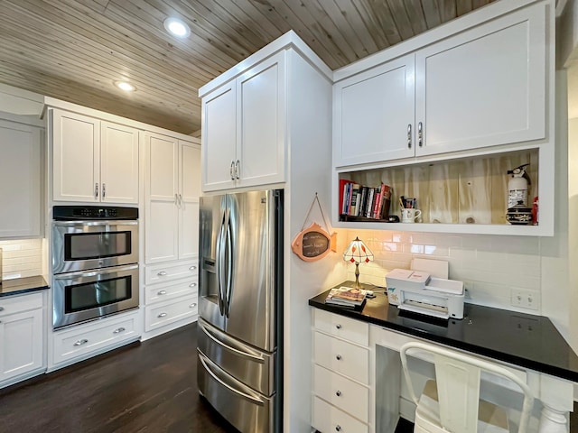 kitchen with built in desk, stainless steel appliances, decorative backsplash, white cabinets, and dark wood-type flooring