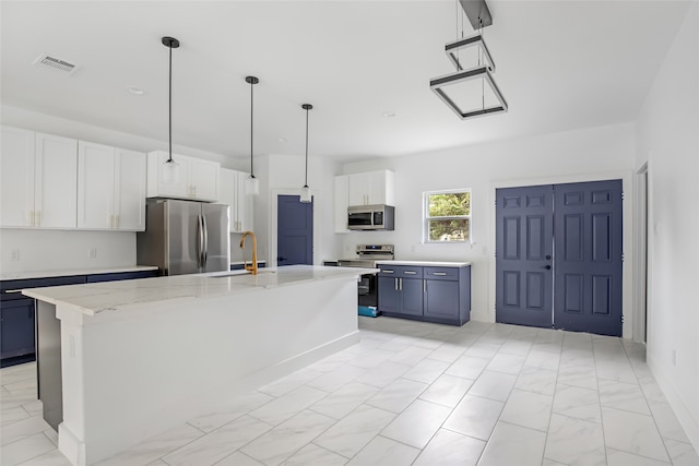 kitchen with stainless steel appliances, sink, a kitchen island with sink, white cabinetry, and decorative light fixtures