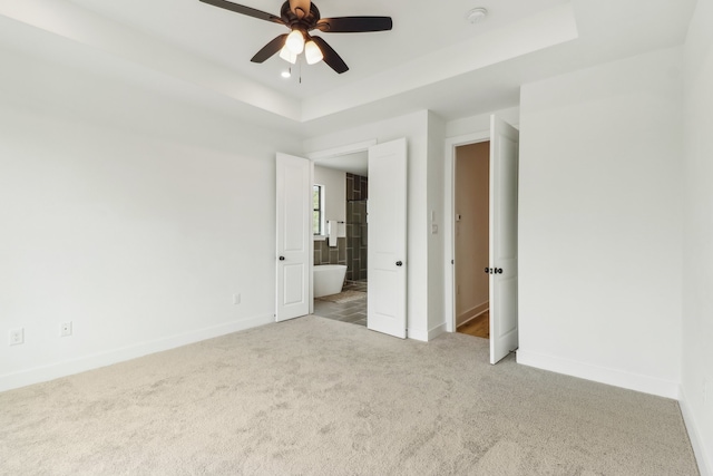 unfurnished room featuring ceiling fan, light colored carpet, and a raised ceiling