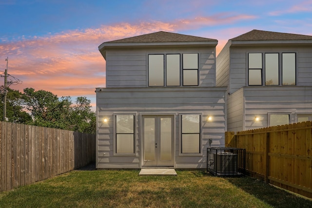 back house at dusk with a lawn, cooling unit, and french doors