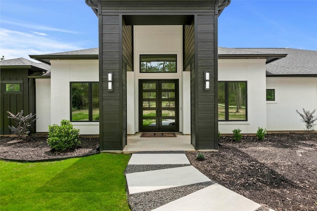 entrance to property with french doors, roof with shingles, and a lawn