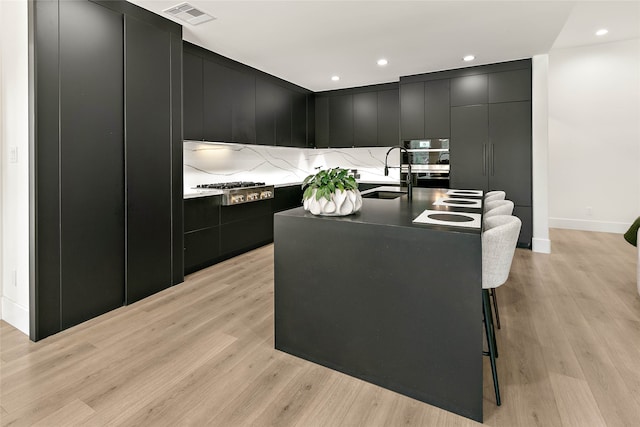 kitchen with stainless steel appliances, a kitchen island with sink, a breakfast bar area, and light hardwood / wood-style flooring