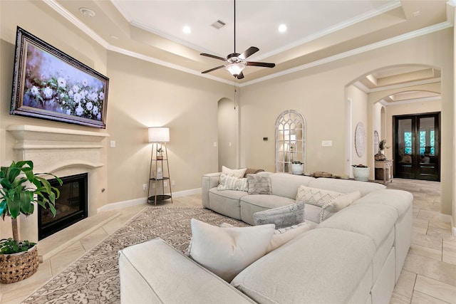 living room with a fireplace, a tray ceiling, ceiling fan, and ornamental molding