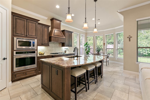 kitchen with light stone counters, an island with sink, a healthy amount of sunlight, and appliances with stainless steel finishes