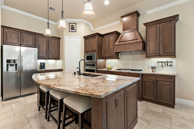 kitchen with premium range hood, a kitchen island with sink, crown molding, sink, and appliances with stainless steel finishes