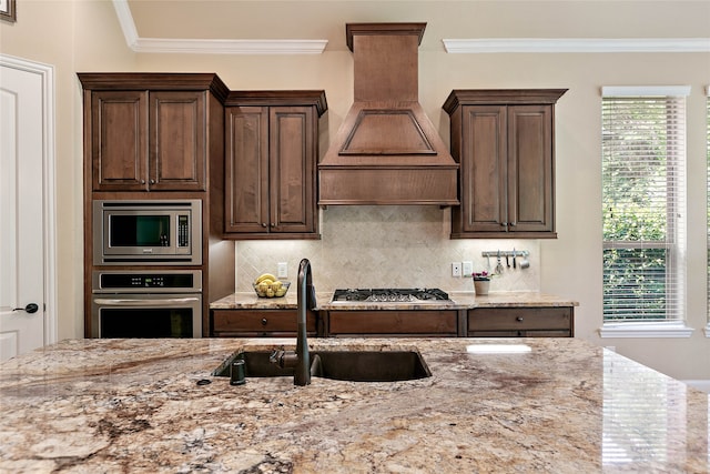 kitchen with light stone countertops, custom range hood, stainless steel appliances, crown molding, and sink