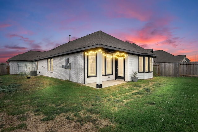 back house at dusk featuring central air condition unit, a patio area, and a lawn