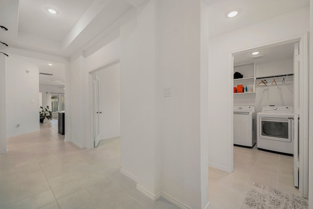 hall with a tray ceiling, washing machine and dryer, and light tile patterned floors