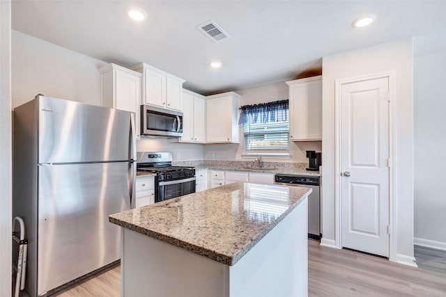 kitchen with white cabinets, stainless steel appliances, light hardwood / wood-style floors, and a kitchen island