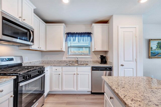 kitchen featuring sink, light stone counters, appliances with stainless steel finishes, light hardwood / wood-style flooring, and white cabinets