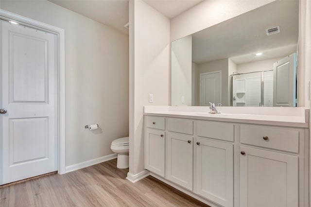 bathroom featuring toilet, vanity, wood-type flooring, and a shower with shower door