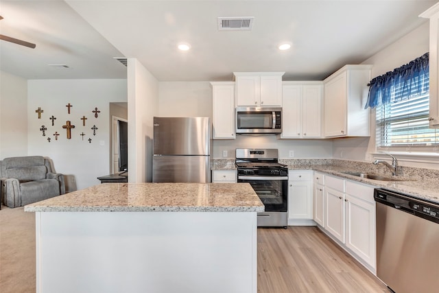 kitchen with light stone counters, white cabinets, sink, light wood-type flooring, and appliances with stainless steel finishes