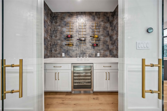 bar with wine cooler, light wood-type flooring, and white cabinets