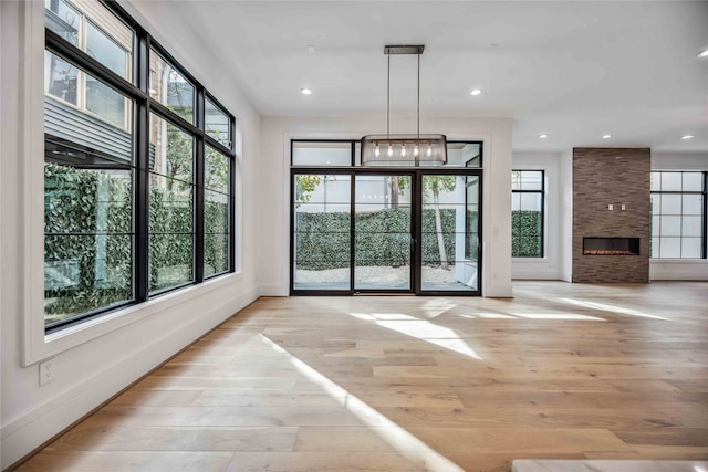 doorway with a stone fireplace, light wood-type flooring, and a notable chandelier