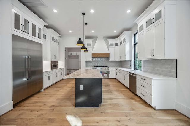 kitchen with a center island, hanging light fixtures, custom range hood, high quality appliances, and light wood-type flooring