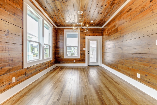 spare room with wood walls, an inviting chandelier, wooden ceiling, and light hardwood / wood-style flooring