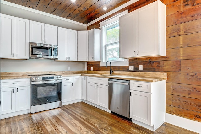 1324 Ursuline St, Galveston, TX 77550 - kitchen featuring stainless steel appliances, wooden ceiling, a sink, wood finished floors, and white cabinetry