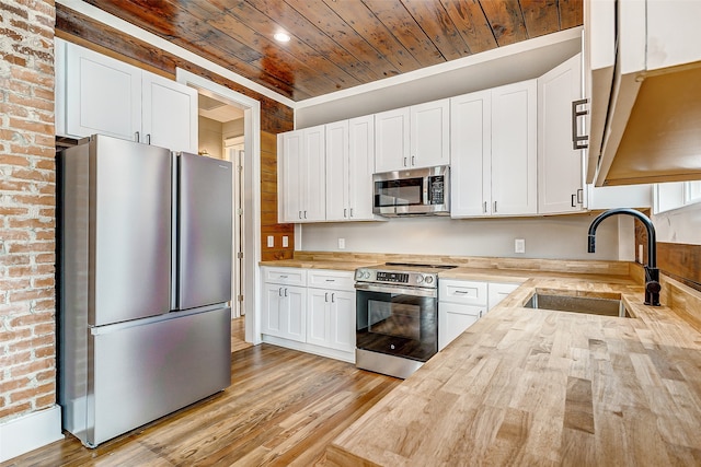 kitchen featuring stainless steel appliances, butcher block counters, white cabinetry, sink, and brick wall