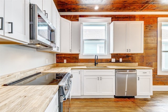 kitchen featuring stainless steel appliances, white cabinetry, wood walls, sink, and light hardwood / wood-style flooring