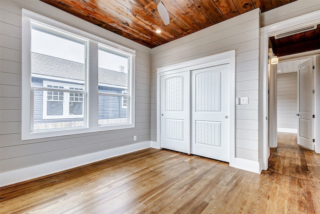 unfurnished bedroom featuring wooden ceiling, ceiling fan, wooden walls, and light wood-type flooring