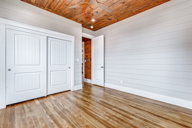 unfurnished bedroom featuring wood ceiling, wooden walls, ceiling fan, a closet, and light hardwood / wood-style flooring