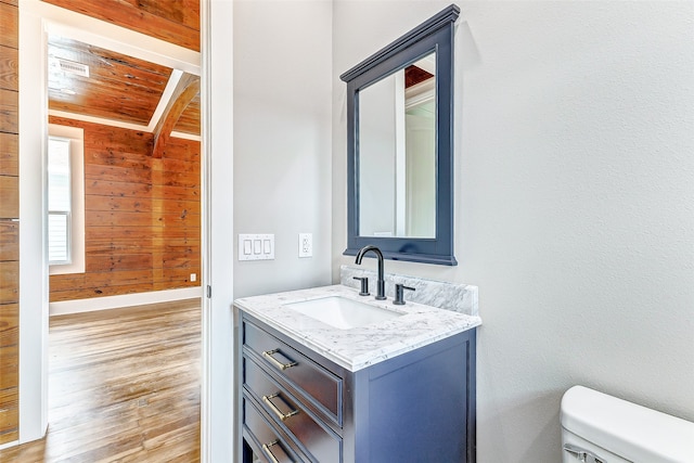 bathroom with toilet, wood walls, wooden ceiling, vanity, and beamed ceiling