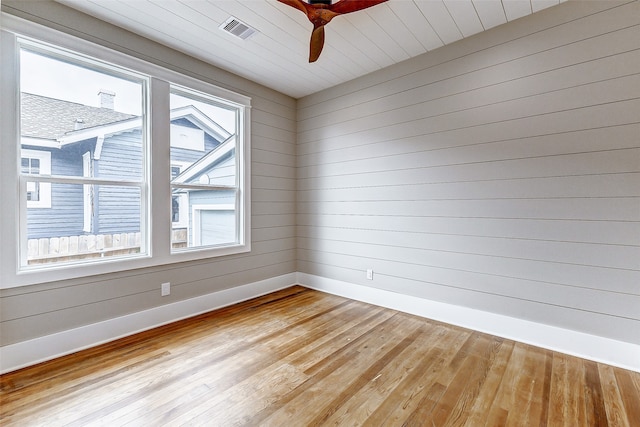 empty room with light hardwood / wood-style floors, a wealth of natural light, and wooden walls