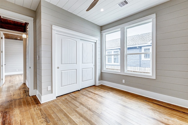 unfurnished bedroom featuring light wood-type flooring, wood walls, ceiling fan, and a closet