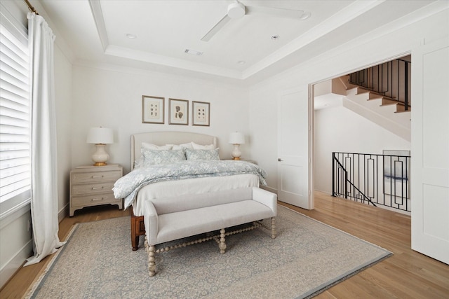 bedroom featuring light hardwood / wood-style floors, ceiling fan, and a tray ceiling