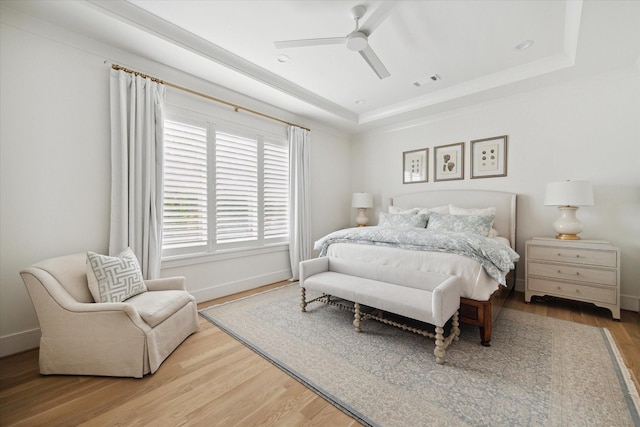 bedroom with hardwood / wood-style floors, ceiling fan, and a raised ceiling