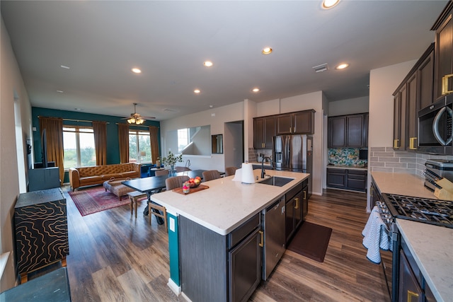 kitchen with stainless steel appliances, a center island with sink, sink, tasteful backsplash, and dark hardwood / wood-style flooring