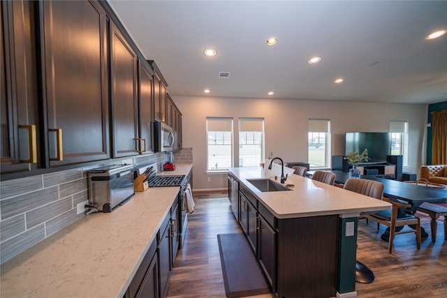 kitchen with a center island with sink, stainless steel appliances, a kitchen bar, decorative backsplash, and sink