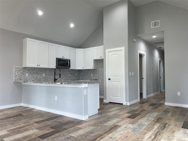 kitchen with tasteful backsplash, wood-type flooring, white cabinetry, high vaulted ceiling, and kitchen peninsula