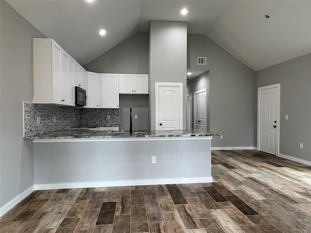 kitchen with dark stone countertops, kitchen peninsula, dark hardwood / wood-style floors, and white cabinets