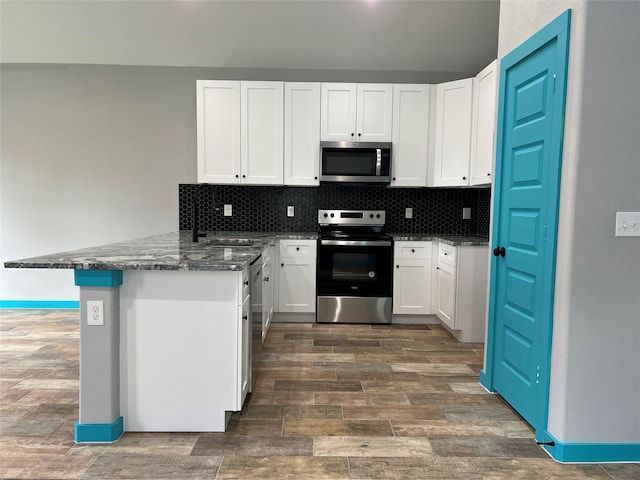 kitchen with tasteful backsplash, appliances with stainless steel finishes, dark hardwood / wood-style floors, white cabinets, and kitchen peninsula