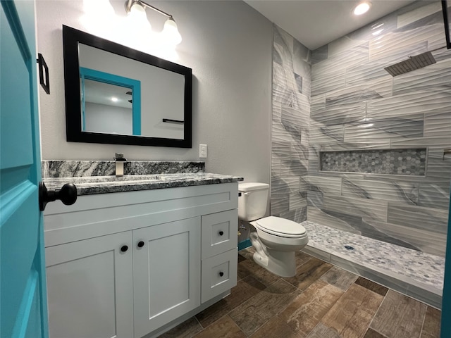 bathroom featuring toilet, vanity, hardwood / wood-style flooring, and tiled shower