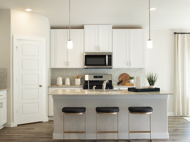 kitchen with a center island with sink, white cabinetry, appliances with stainless steel finishes, dark hardwood / wood-style flooring, and hanging light fixtures