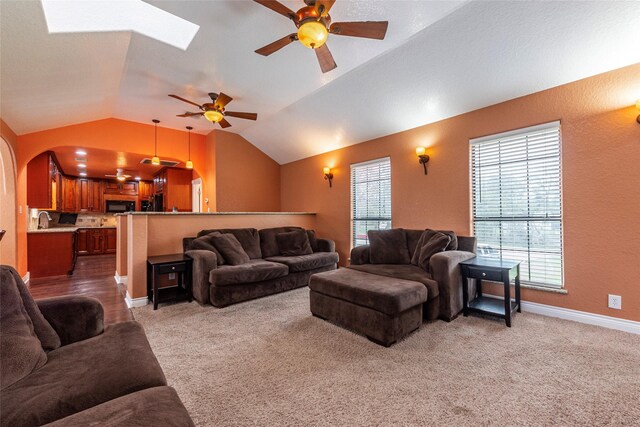 carpeted living room featuring ceiling fan, sink, and lofted ceiling with skylight