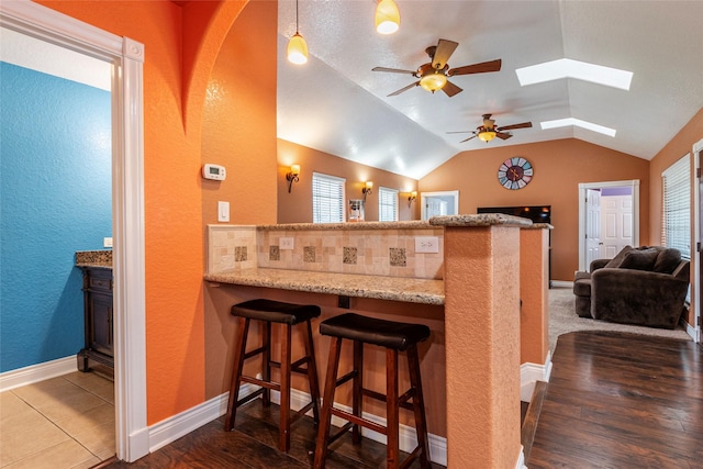 kitchen featuring light stone countertops, vaulted ceiling with skylight, wood-type flooring, kitchen peninsula, and a breakfast bar