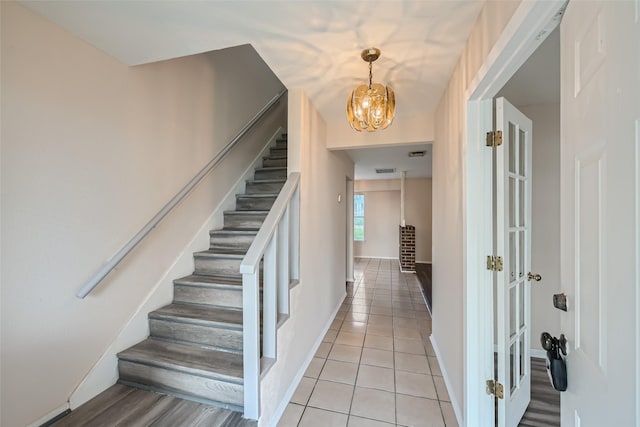 stairway with tile patterned flooring and a notable chandelier