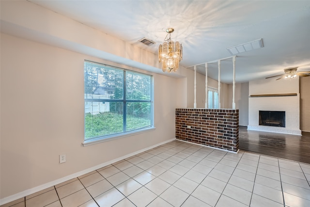 empty room with ceiling fan with notable chandelier, light hardwood / wood-style floors, and a brick fireplace