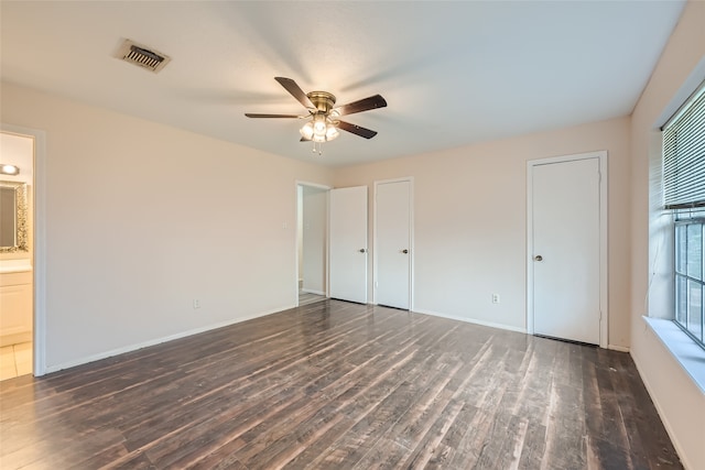 unfurnished bedroom with dark hardwood / wood-style flooring, connected bathroom, ceiling fan, and multiple closets