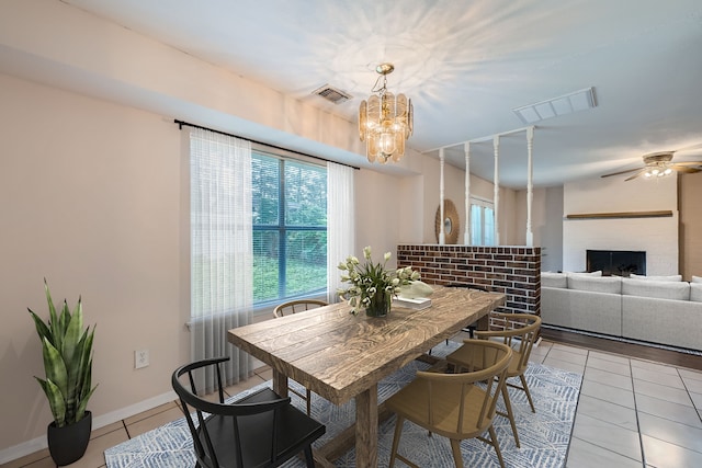 tiled dining space featuring ceiling fan with notable chandelier and a brick fireplace